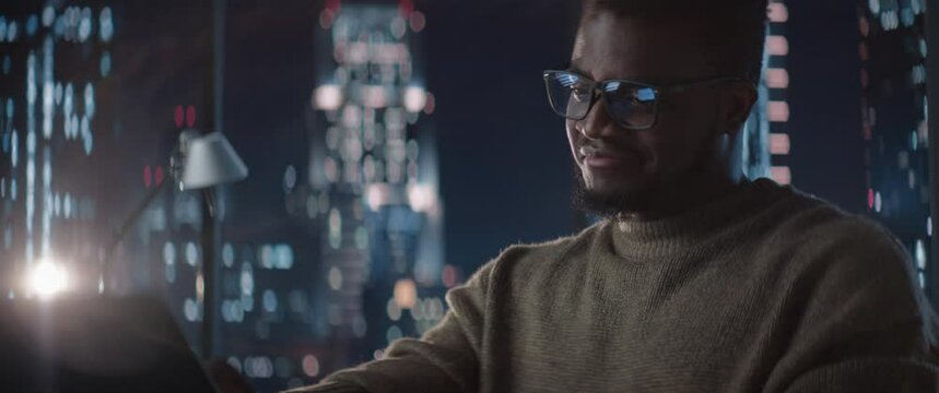 Close Up Of Successful Handsome Black Businessman Working on Laptop in Big City Office Late at Night. African Corporate Manager Checking Financial Data from Project Management Report. Anamorphic Shot