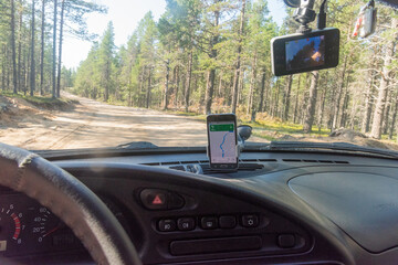 view from inside an off-road car on a country road in the forest in summer, on the dashboard of the car is a mobile navigator with an electronic map