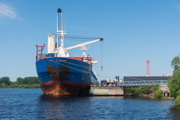 a marine vessel carries out loading at the pier. against the background of blue sky and green coast