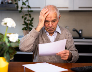 Old gray haired man sitting at table and stunned notice on white sheet