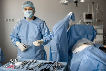 Portrait of a surgeon in uniform with sterile medical instruments ready for surgery in the...