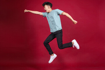 Full length ttractive young guy jumping to the side like superhero on crimson background