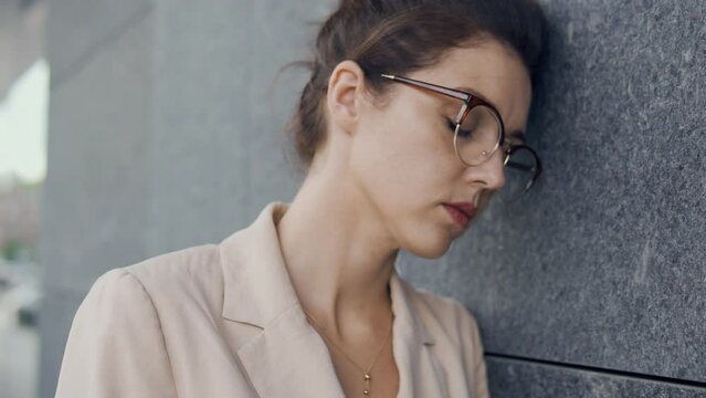 Overworked woman leaning on wall of building outdoor, has no energy to go home