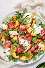Healthy summer salad with peach, burrata, arugula and jamon. Healthy eating.