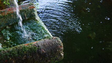 Coulée d'eau ou ruisseau d'eau sur de la pierre, dans la nature, source d'eau, abondance, ambiance zen, tranquille, coloration verte et marronne, avec réflexion de lumière de miroir, beauté aquatique 