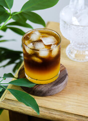 Bumble coffee banner with tropical leaves background. Coffee with orange juice. Trendy coffee drink made of orange juice, espresso, caramel syrup and ice cubes. Layered coffee cocktail, wooden table