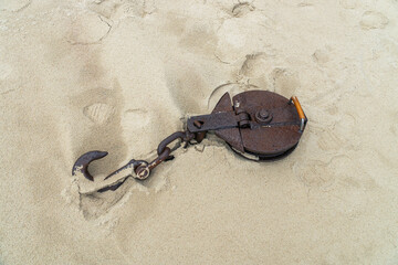 The rusty iron hook of a ship winch lies on the sand of the coast.
