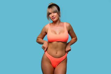 Naklejka premium Slim woman posing wearing orange swimsuit on blue background