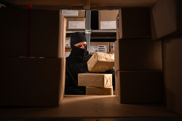 Thief in black balaclava steals with a parcel in a warehouse at the night. Concept of security...
