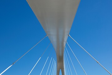White modern steel cable bridge against blue sky.