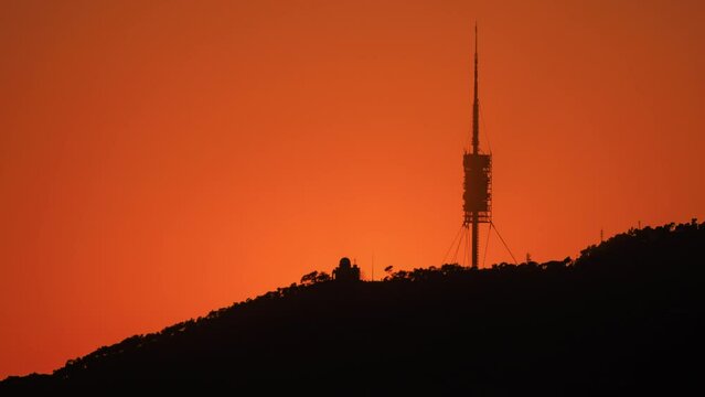 Setting sun (sunset) over Barcelona city skyline, Tibidabo mountain, and Collserola TV tower, Spain