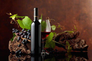 Glass and bottle of red wine with blue grapes and vine branches.