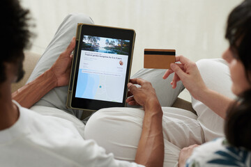 Above angle of young intercultural couple with tablet and credit card sitting next to one another and paying for online travel service