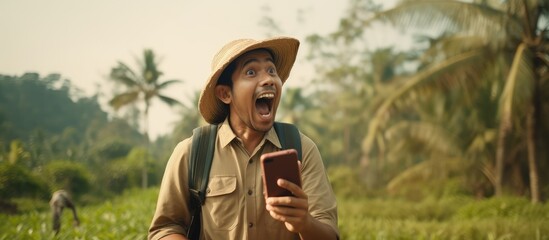 Indonesian farmer in traditional attire with suitcase smiling happily and looking shocked during a video call on smartphone - obrazy, fototapety, plakaty