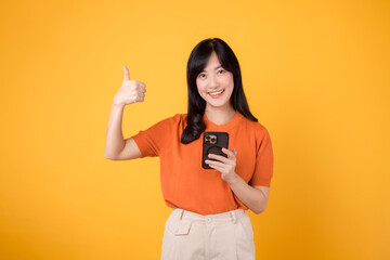 Smiling Asian woman in her 30s, wearing orange shirt, using smartphone with thumb up hand sign on...