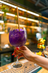 close-up of a hand holding a freshly made purple alcoholic cocktail with passion fruit seeds in a...