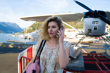Woman tourist talking on phone, summer fashion style, travel to Europe. Fashion tourist. Elegant woman tourist in trendy dress near jet. Travel tourist in Como lake Italy.