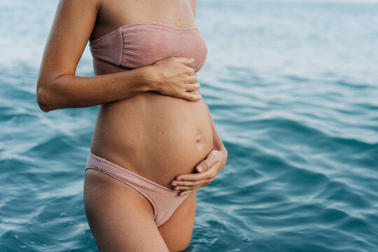Portrait of an unrecognizable pregnant woman in a swimsuit on the seashore.