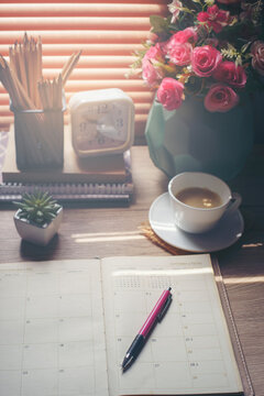 Agenda, planner book, calendar, cup of coffee, pencil, and clock placed on business office desk in morning. Diary for organizer to plan timetable, daily appointment, and management job in work room.