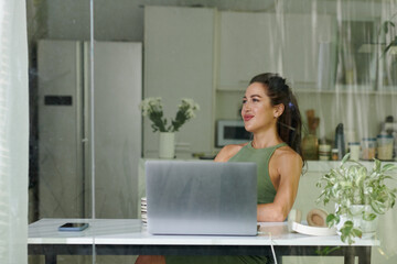 Fototapeta na wymiar Young restful brunette woman sitting by desk in front of laptop in home environment, enjoying short break and thinking about something