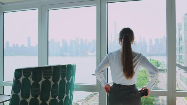 Young successful businesswoman in office wearing nice suit going to window for inspiration. Classy pretty young Caucasian female worker working at modern company office.