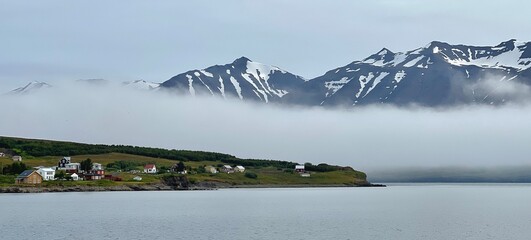 Hrisey Island under the snowy mountains and fog in Eyjafjordur, Iceland