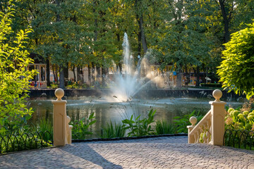 Picturesque pond with a fountain and trees in a city garden on a summer day