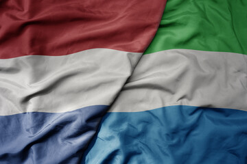 big waving national colorful flag of netherlands and national flag of sierra leone .