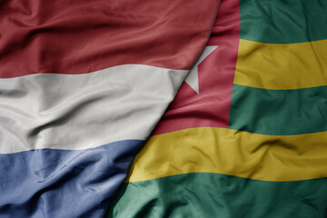 big waving national colorful flag of netherlands and national flag of togo .