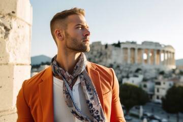 Photography in the style of pensive portraiture of a grinning boy in his 30s wearing a bold statement necklace in front of the acropolis in athens greece. With generative AI technology