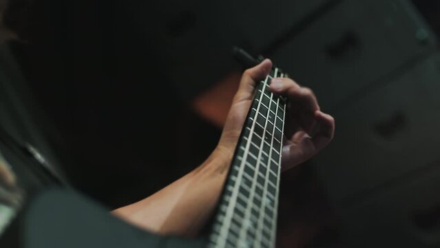A close-up of a talanted musician playing an electric guitar passionately and quickly, plucking strings, illuminated by warm light in a studio