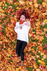 Woman lying on ground covered with autumn leaves, above view