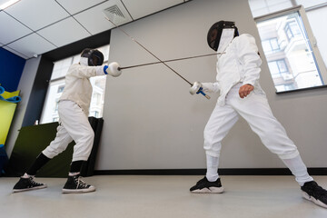 Portrait of kids and adults fencers with trainer engaged in fencing in training room