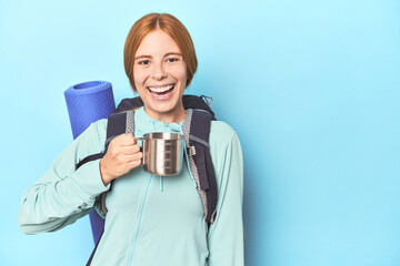 Mountaineer redhead sipping from camping cup in blue studio