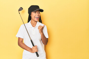 Indonesian female golfer on yellow backdrop points with thumb finger away, laughing and carefree.