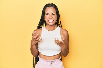Young Indonesian woman on yellow studio backdrop upset screaming with tense hands.