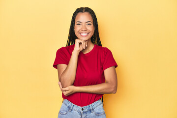 Young Indonesian woman on yellow studio backdrop smiling happy and confident, touching chin with hand.