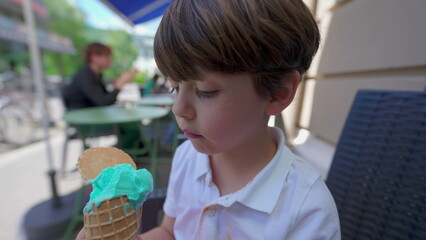 Little Boy Savors Ice-Cream cone on a Summer Day. Child licking colorful blue icecream outside