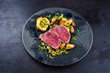 Fried Italian chianina beef fillet steak very rare with mushrooms, chopped pistachios and Beignet served as close-up in a Nordic design plate with copy space