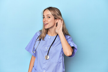 Young caucasian nurse in blue studio trying to listening a gossip.