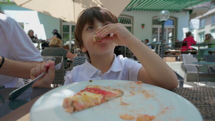 Small boy eating pizza at restaurant, child treating himself carb food for lunch