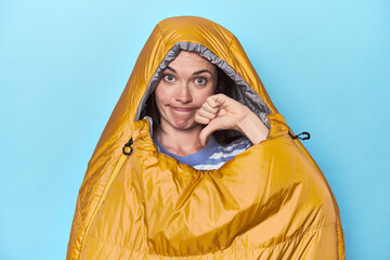 Woman in sleeping bag on blue background showing a dislike gesture, thumbs down. Disagreement...