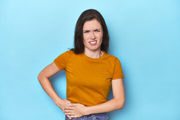 Fototapeta premium Young caucasian woman on blue backdrop having a liver pain, stomach ache.