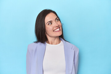 Obraz premium Woman in blue blazer on blue background relaxed and happy laughing, neck stretched showing teeth.