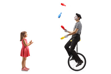 Full length profile shot of a girl clapping and looking at a mime juggling and riding a unicycle
