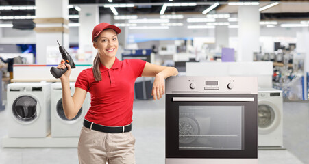 Repairwoman with a drill standing next to an oven
