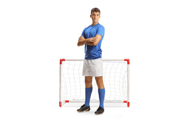 Full length portrait of a young football player in a blue jersey posing with folded arms in front...