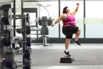 Full length profile shot of an overweight woman exercising step aerobics in a gym