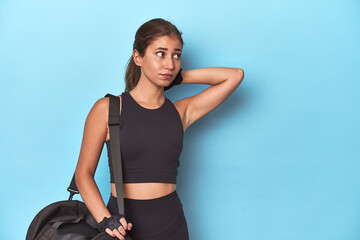 Sporty teen with gym bag, ready for a workout touching back of head, thinking and making a choice.