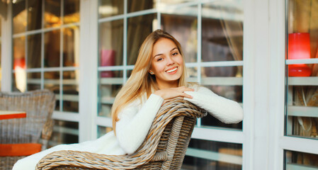 Portrait of beautiful blonde smiling young woman sitting on chair waiting in city cafe